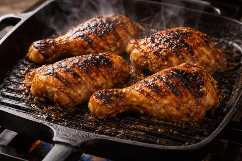 Potongan ayam sedang dibakar di atas grill atau dalam oven, kulit mula perang keemasan dengan char marks