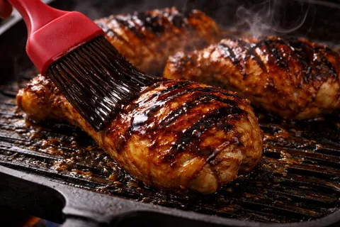 Berus masak menyapukan sos perapan perang berkilat ke atas ayam yang sedang dibakar, kulit berkilat dan perang karamel
