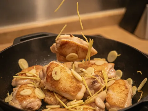 Ketul ayam ditumis bersama halia dan bawang putih dalam kuali sehingga bertukar warna