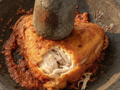 Ketul ayam goreng dipenyet dengan anak lesung di atas sambal belacan merah dalam cobek batu