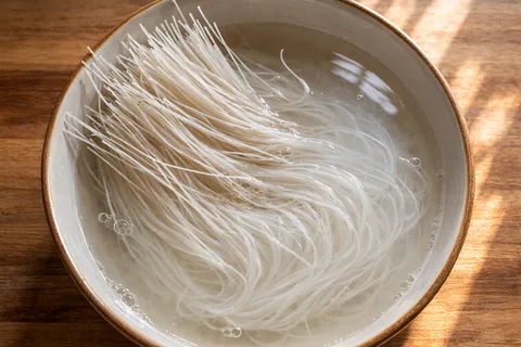 Bihun kering direndam dalam air separuh panas dengan sedikit minyak dalam mangkuk besar