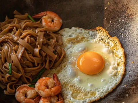 Telur dipecahkan di tepi kuali di sebelah kuey teow, tepi telur garing berenda sebelum digaul bersama mi