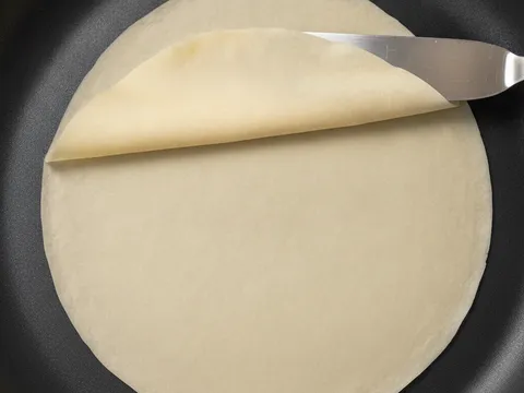 Sekeping kulit popia siap masak dicungkil dari tepi kuali dan ditarik keluar dalam satu gerakan