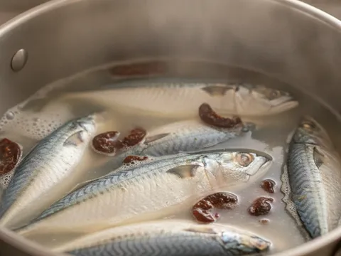 Ikan kembung direbus bersama asam keping dalam periuk besar, buih dibuang dari permukaan
