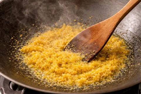 Bahan kisar kuning ditumis dalam periuk besar sehingga terbit minyak