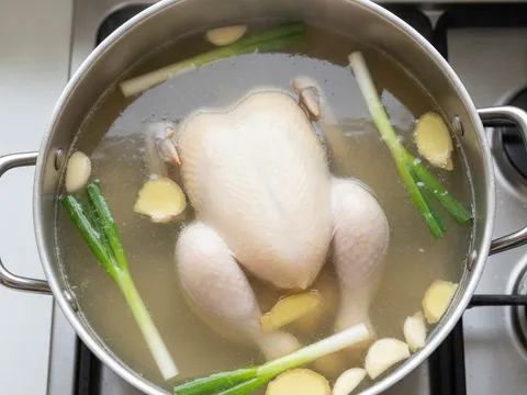 Seekor ayam direbus perlahan dalam periuk besar bersama halia, bawang putih dan daun bawang