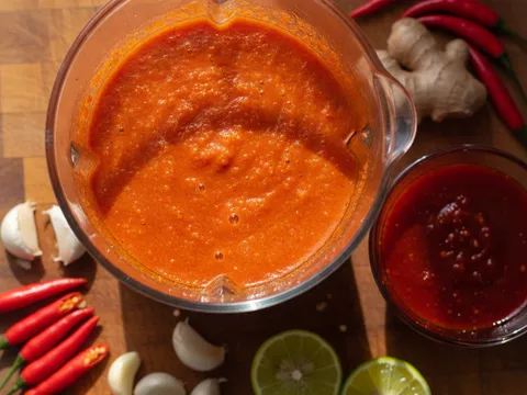 Sos cili nasi ayam merah terang dikisar halus dalam blender dengan halia, bawang putih dan limau nipis