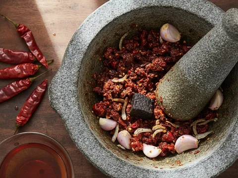 Cili kering, bawang merah, bawang putih dan ikan bilis ditumbuk kasar dalam lesung batu