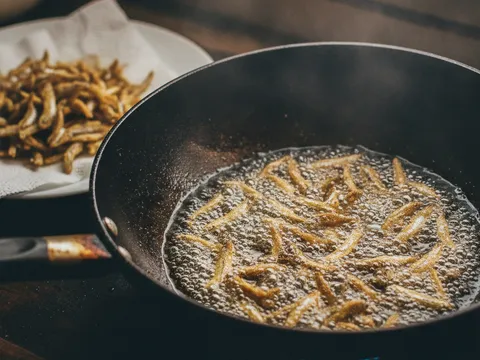 Ikan bilis digoreng keemasan dan rangup dalam kuali, ditoskan di atas tisu dapur