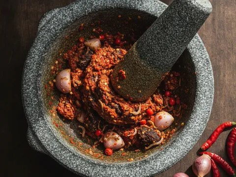 Sambal cili kering, bawang, belacan dan ikan bilis ditumbuk kasar dalam lesung batu