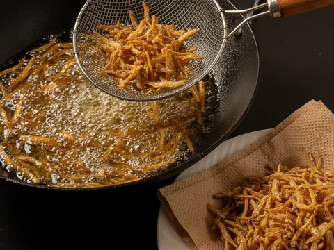 Ikan bilis digoreng keemasan dan rangup dalam kuali minyak panas