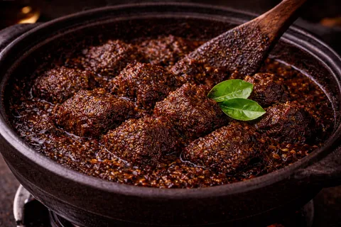 Daun limau purut dimasukkan ke rendang coklat gelap yang hampir kering