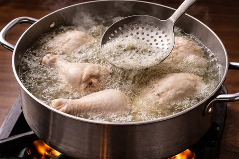 Ayam direbus dalam periuk besar menghasilkan stok kuning bening untuk soto ayam