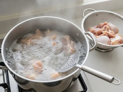 Potongan ayam dicelur dalam air mendidih, buih kelabu naik ke permukaan sebelum ditapis dan dibilas